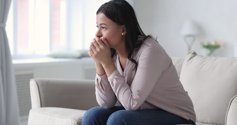 Frustrated african ethnicity young woman sitting on couch, thinking of personal problems alone at home. Depressed unhappy mixed race lady suffering from mental stress, feeling unsure of decision.