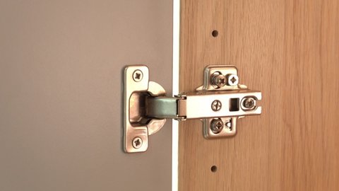 Close up male hand tightens screw with screwdriver on a polished stainless door hinge on a cabinet door. Craftsman repairing home furniture.