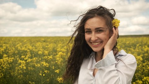 Happy girl in spring yellow rape poses in front of the camera and sincerely smiles