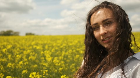 Cheerful girl of Caucasian appearance in rapeseed. Enjoys the nature of yellow flowers