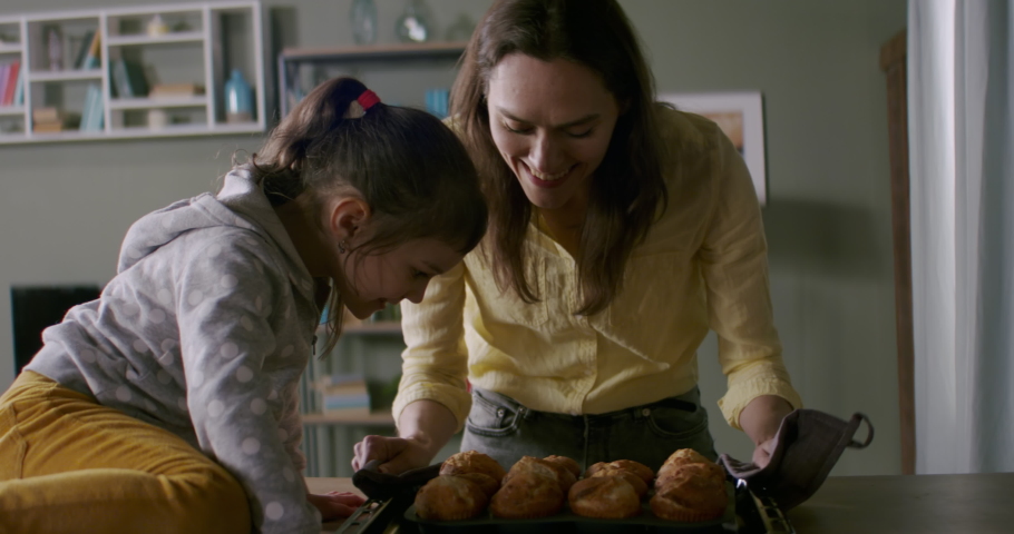 Mother and daughter cooking together at home, taking out bakery from the oven in the kitchen