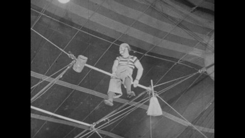 1940s: 2 clowns on aerial bars swing, wrap around each other, one sweeps the butt of other, spanks with broom, they flip, clown kicks butt of other clown, hits butt with exploding mallet, clown falls
