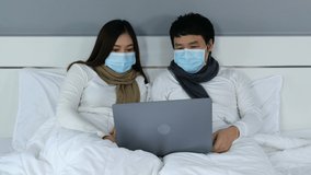 couple with medical masks using laptop on a bed during quarantine pandemic coronavirus(covid-19) stay at home. 4k video

