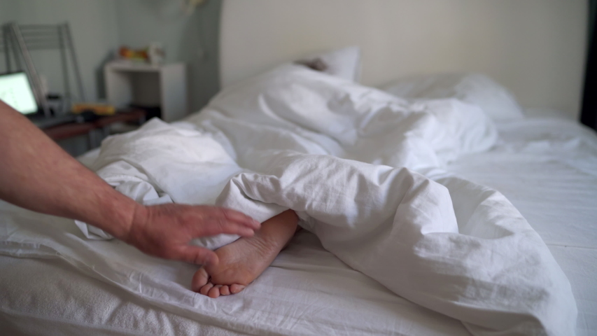 Woman sleeping in bed under white blanket, man touching womans bare feet. | Shutterstock HD Video #1053330908