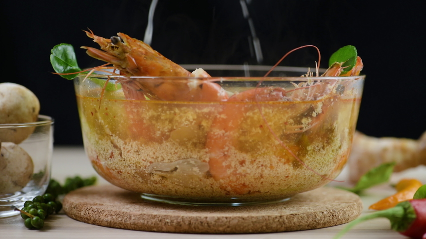 Tom Yam Kung or Tom Yum soup is Thai hot spicy soup shrimp or prawn with lemon grass, lemon, galangal, mushrooms, coconut milk and chili in bowl on wooden table top view, famous Thai food cuisine.