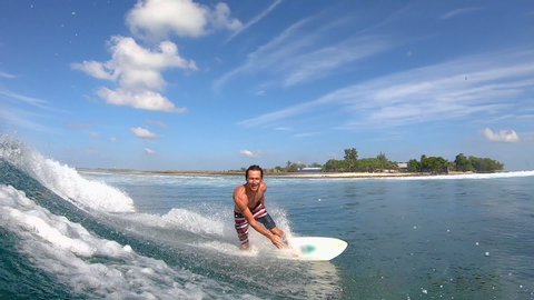 SLOW MOTION, PORTRAIT: Cheerful Caucasian surfer gives the shaka while riding a fun wave. Stoked male tourist on vacation in the Maldives surfs on a sunny summer day. Surfer riding glassy waves.