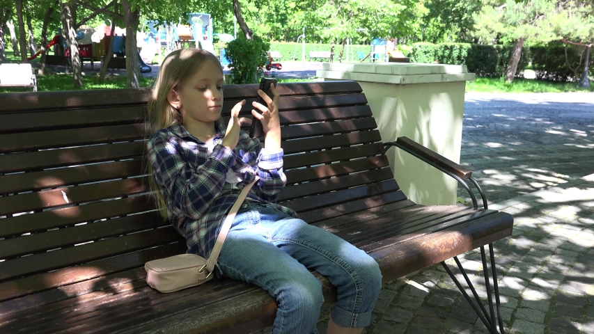Kid Playing Smartphone Browsing Internet at Playground in Park, Girl Sitting on Bench, Child Outdoor in Park