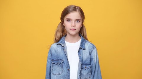 Little blonde kid teen teenager girl 12-13 years old in denim jacket white t-shirt posing isolated on yellow background studio. People childhood lifestyle concept Looking at camera with charming smile