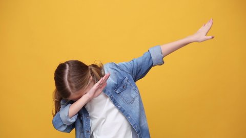 Little fun blonde kid teen teenager girl 12-13 years old in denim jacket white t-shirt posing isolated on yellow background studio. People childhood lifestyle concept showing doing DAB dance gesture