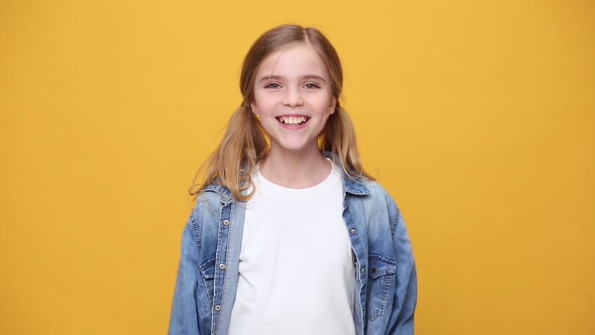 Little fun blonde kid teen teenager girl 12-13 years old in denim jacket white t-shirt posing isolated on yellow background studio People childhood lifestyle concept Dancing waving hand fooling around Royalty-Free Stock Footage #1053333614