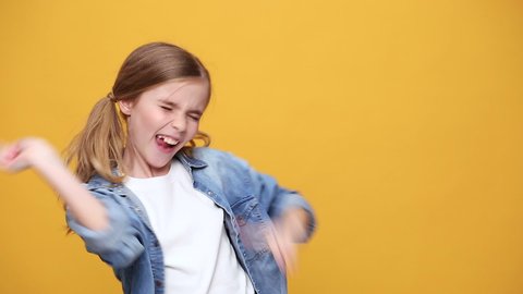 Little fun blonde kid teen teenager girl 12-13 years old in denim jacket white t-shirt posing isolated on yellow background studio People childhood lifestyle concept Dancing waving hand fooling around