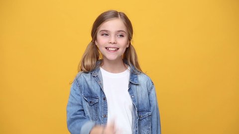 Little kid teen girl 12-13 years old in denim jacket white t-shirt posing saying hush be quiet with finger on lips shhh gesture isolated on yellow background studio. People childhood lifestyle concept