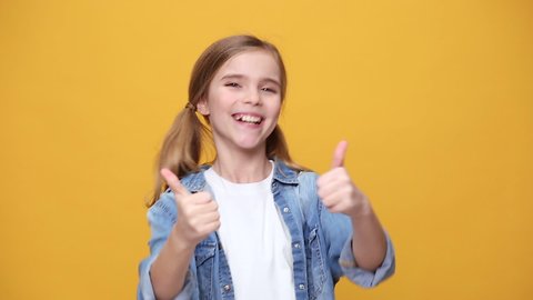 Little kid teen girl 12-13 years old in denim jacket white t-shirt posing isolated on yellow background studio. People childhood lifestyle concept Looking at camera say you are cool showing thumbs up