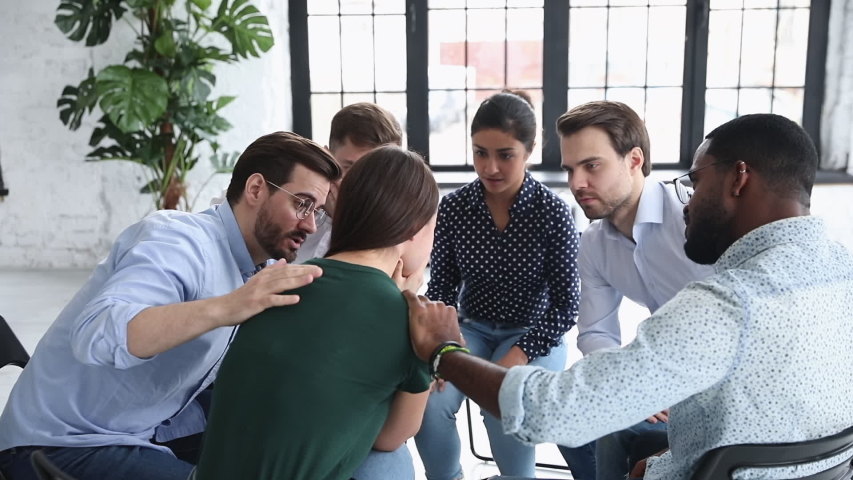 Compassionate multiracial business people supporting depressed woman, sitting on chairs in circle at psychotherapy meeting in office. Supportive diverse employees comforting desperate crying colleague | Shutterstock HD Video #1053336197