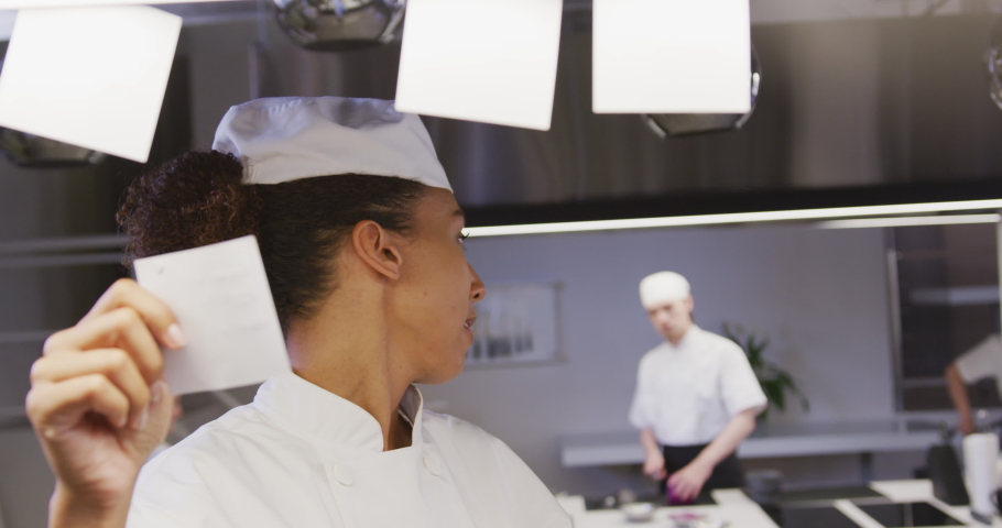 An African American female chef working in a busy restaurant kitchen, checking orders, with colleagues working in the background in slow motion Royalty-Free Stock Footage #1053336566