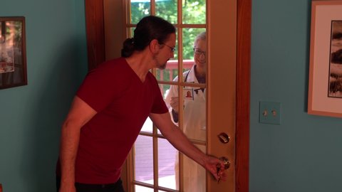 Mature woman nurse or doctor at home door knocking, showing badge, greeting, and entering.