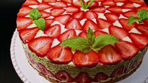 Amazing beautiful hand decorated homemade strawberry Fraisier cake rotates. Tasty, fresh, appetizing dessert close-up with sprigs of mint. Confectionery art, perfectionism in food concept.