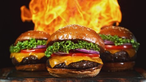 Tasty cheeseburger, lying on vintage wooden cutting board with fire flames in background. Super Slow motion filmed on cinema camera at 1000 fps