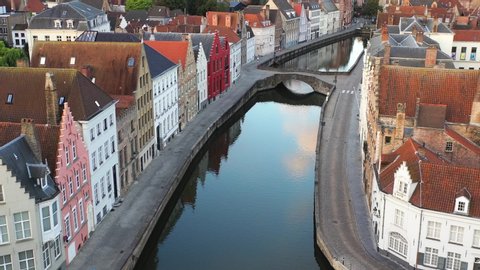 Low aerial fly over Bruges famous canals with a pan up reveal of the architecture and historic buildings of the city including the Belfry bell tower.