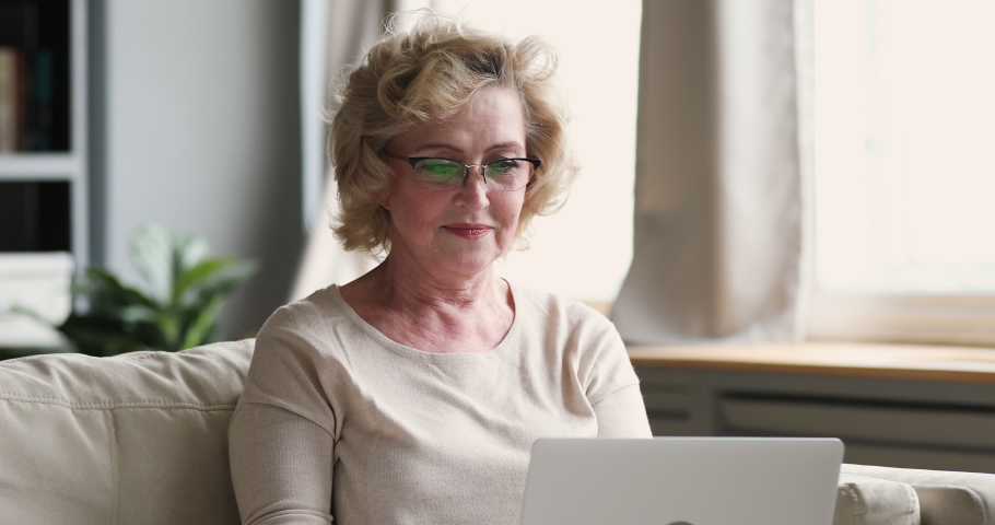 Head shot happy elderly grandmother looking at computer screen, enjoying chatting with friends or web surfing information. Smiling beautiful older woman using laptop, spending weekend time online. Royalty-Free Stock Footage #1053347495