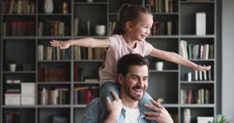 Head shot smiling young father holding on shoulders happy playful small preschool kid daughter, having fun together at home. Cheerful millennial daddy playing airplane with little cute child girl.