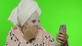 Adult senior caucasian woman grandmother in bathrobe and cosmetic face mask on face using smartphone social network app for video call. Chroma key. Beauty procedures for mature grandparents people