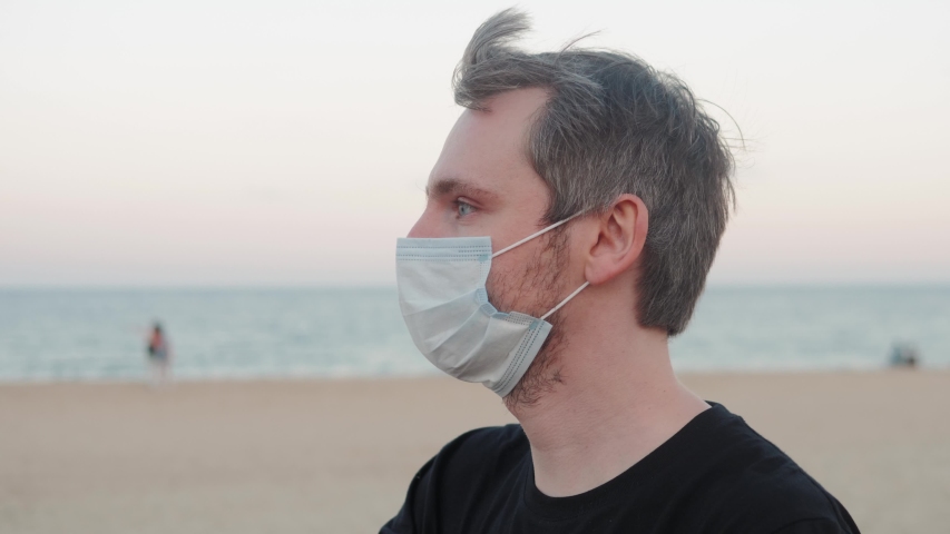 Man taking off mask after coronavirus quarantine is over, happy tourist drinking beer in bar on beach, the end of lockdown, first days after pandemic, happy student near sea.