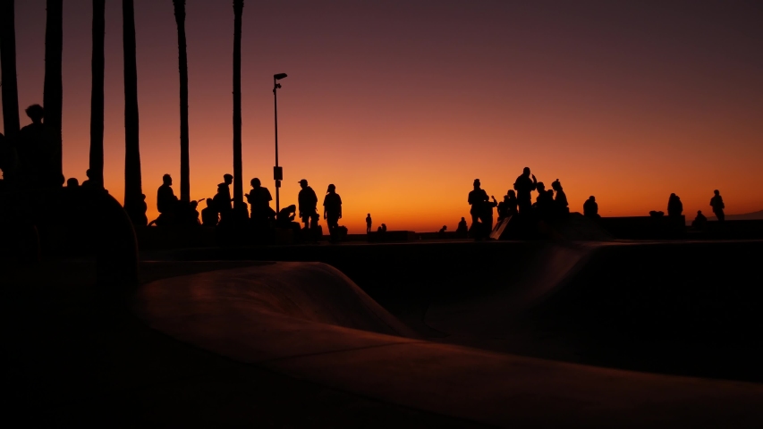 Silhouette of young jumping skateboarder riding longboard, summer sunset background. Venice Ocean Beach skatepark, Los Angeles California. Teens on skateboard ramp, extreme park. Group of teenagers