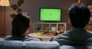Couple spending time together in the evening, sitting on couch and watching tv with green chroma-key green screen. A template for your clips 4k footage