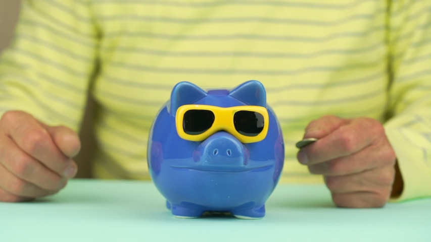 blurry aged man in yellow pullover throws coins into piggy bank and hugs putting head with glasses slow motion closeup