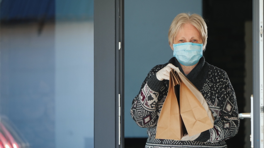 An elderly woman with bags of food on the doorstep of her home
