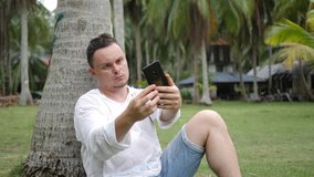Male Office Worker Using Smartphone Take Selfie. Take picture of yourself. Man sits on green grass near palm tree on green background