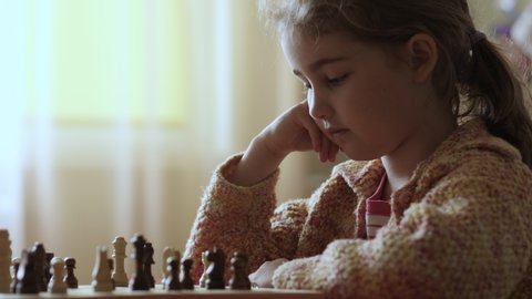 Portrait of Smart Little Girl Playing Chess. Child Playing Chess With Friend at Home, Development of Logical Thinking for Children. Intellect, Intelligence. Development Logical Thinking. Slow Motion.