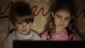 Portrait Сute Little Kids While Watching TV on Laptop. Boy and Girl Watch Cartoon on Laptop on Living Room. Concept Video Game, Entertainment, Emotions, Family. Children Brother and Sister Watching TV