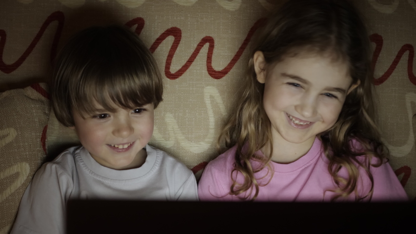 Portrait Сute Little Kids While Watching TV on Laptop. Boy and Girl Watch Cartoon on Laptop on Living Room. Concept Video Game, Entertainment, Emotions, Family. Children Brother and Sister Watching TV | Shutterstock HD Video #1053364385