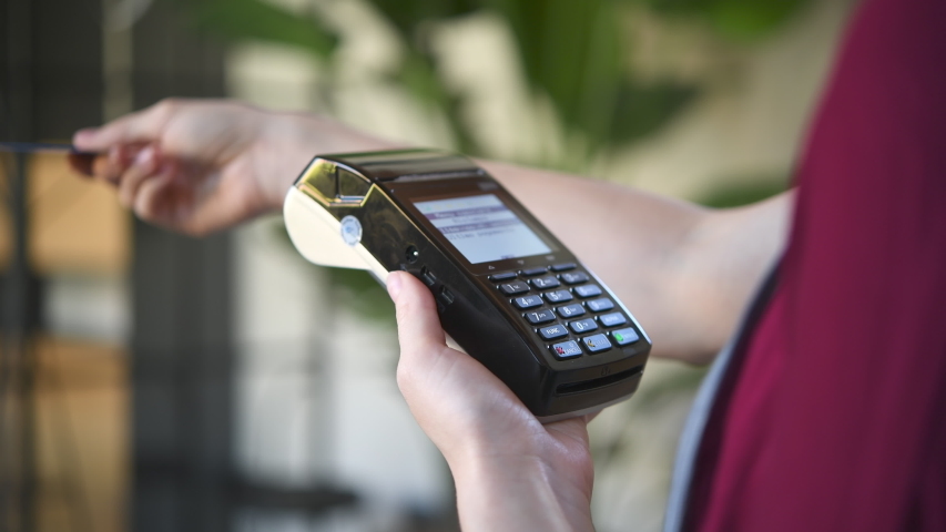 Close up of woman hands making a credit card payment with card reader machine. Credit card swipe through terminal for sale in store. Cashier hand swiping debit card after a purchase. | Shutterstock HD Video #1053365423