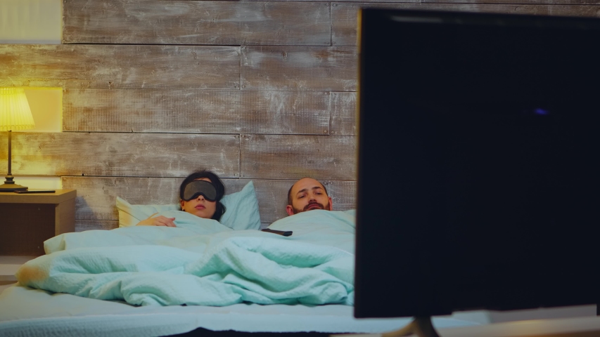 Young couple in bedroom falling asleep in fron of tv