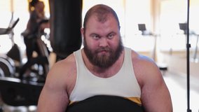 Very large bearded bodybuilder trains legs in the gym.