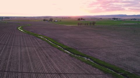 Flying over small canal cutting through farmers field in Idaho during sunset.