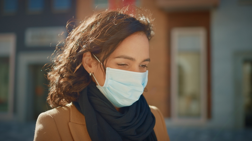 Portrait of a Beautiful Dark Haired Young Woman Wearing Protective Medical Face Mask and Standing on the Street. Safe and Happy Woman Practicing Social Distancing, Quarantine. Blurred City Background | Shutterstock HD Video #1053374318