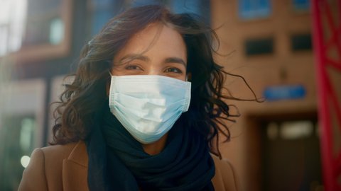 Portrait of a Beautiful Dark Haired Young Woman Wearing Protective Medical Face Mask and Standing on the Street. Safe and Happy Woman Practicing Social Distancing, Quarantine. Blurred City Background