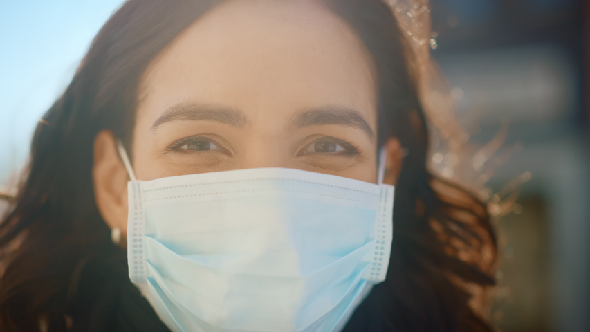 Portrait of a Beautiful Dark Haired Young Woman Wearing Protective Medical Face Mask and Standing on the Street. Safe and Happy Woman Practicing Social Distancing, Quarantine, Air Pollution. Close-up  Royalty-Free Stock Footage #1053374342