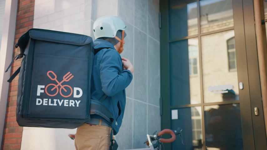Happy Food Delivery Man Wearing Thermal Backpack on a Bike Delivers Restaurant Order to a Beautiful Female Customer. Courier Delivers Takeaway Lunch to Gorgeous Girl in Modern City Center. Slow Motion | Shutterstock HD Video #1053374399