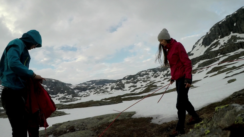 A young couple putting up the tent in the nearby of Trolltunga, Norway. Wild camping in the nature. Couple is having fun. They are surrounded by snow. Winter mountain climbing. Freedom and adventure. 
