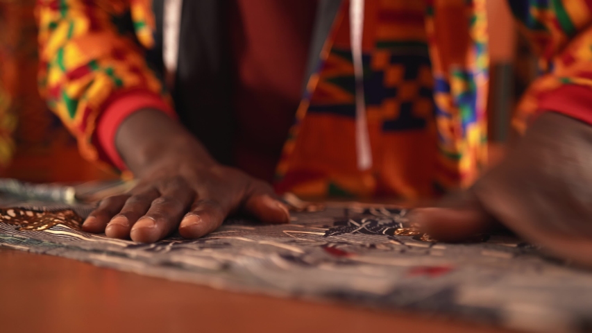 Unrecognizable crop African American tailor in orange jacket cutting blue textile with scissors while working in sewing workshop on daytime | Shutterstock HD Video #1053379847