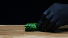 The cook in the kitchen in black gloves cuts cucumbers with a knife. The footage was shot in slow motion