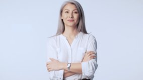 A smiling good-looking old mature woman with long gray hair wearing formal business clothes is doing a thumb up gesture with both hands standing isolated over white background in studio