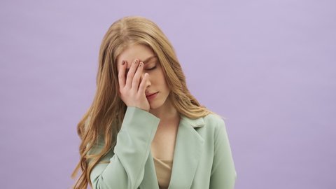 A bored young woman is doing a face palm gesture standing isolated over gray background