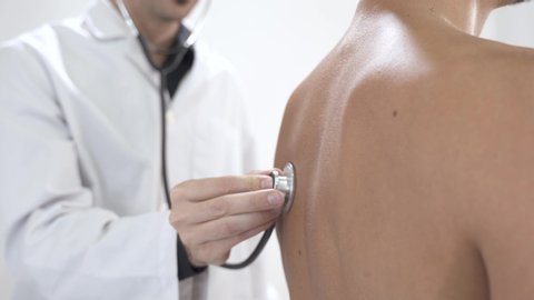 Close up view of doctor using stethoscope while examining patient in hospital. Hand holding stethoscope on clear background. Patient's back examination. Breath respiratory disease.