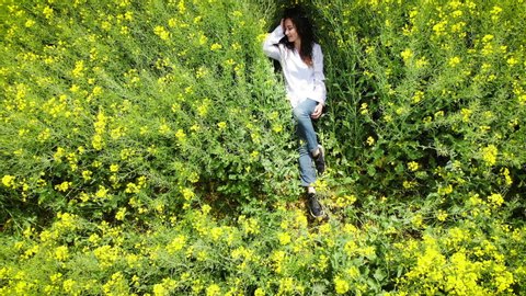 Happy woman of Caucasian appearance lies in a blooming yellow-green field. Spring rape. Drone flight over beautiful nature. Landscapes of Europe